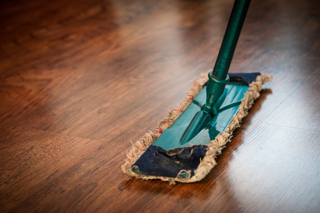 services-03 A detailed view of a mop cleaning a wooden floor, showing texture and pattern.